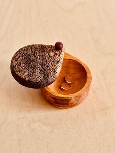 a wooden box with two rings in it on top of a table next to a pair of earrings