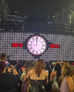 a group of people standing in front of a stage with a large clock on it