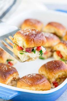 a fork is lifting up some food out of a casserole dish with mini sliders in it