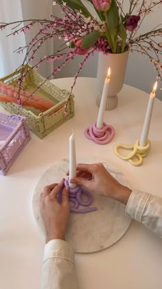 a woman is cutting paper with scissors on a table next to some flowers and candles