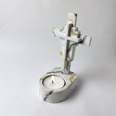 a white candle holder with a cross on it and a lit candle in the middle