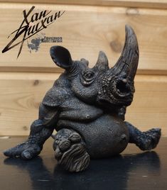 a rhinoceros figurine sitting on top of a black table next to a wooden wall