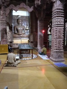 two men are sitting on the floor in front of an intricately decorated room with columns