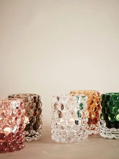 four different colored glass vases sitting next to each other on a table with a white wall in the background