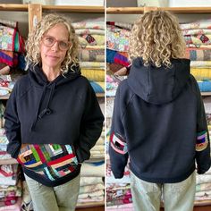 a woman standing in front of a pile of quilts wearing a black hoodie