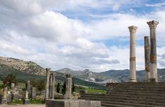 the ruins of an ancient city with columns and stone steps leading up to them on a cloudy day