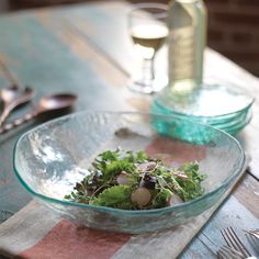 a glass bowl filled with salad on top of a wooden table next to a bottle of wine