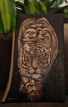 a painting of a tiger on a piece of wood next to a potted plant