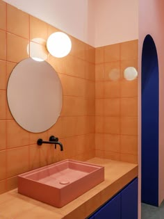 a bathroom with orange and pink tiles on the walls, blue cabinets and a round mirror