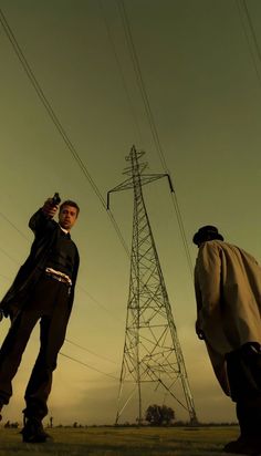 two men standing next to each other in front of power lines and high voltage towers