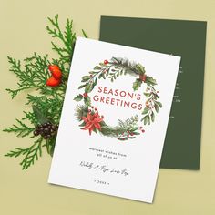 a christmas card on top of a table next to pine cones and holly wreaths