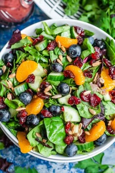 a salad with oranges, blueberries and spinach in a white bowl on a table