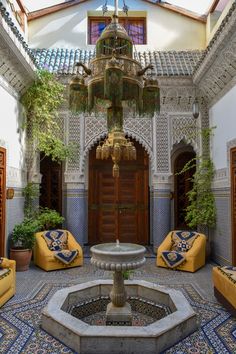 an ornate courtyard with yellow couches and potted plants in the center, surrounded by blue tiles