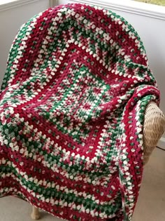 a red and green crocheted blanket sitting on top of a chair next to a window