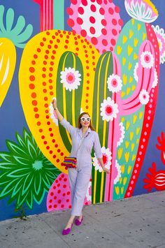 a woman standing in front of a colorful wall with flowers and cacti on it