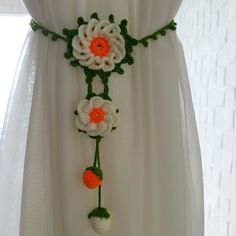 a white curtain with crocheted flowers hanging from it's side and an orange center piece