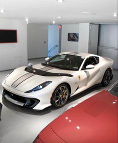 a white sports car parked in a garage next to two red sports cars on display