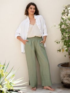 a woman standing in front of a white wall wearing green pants and a white shirt