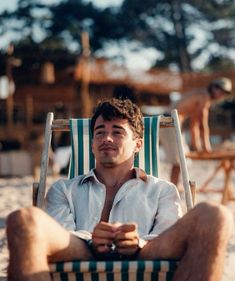 a man sitting in a lawn chair on the beach with his feet crossed and eyes closed