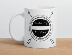 a white coffee mug sitting on top of a wooden table with the words probably whiskey printed on it