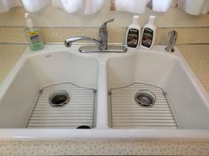 two sinks with soap and lotion in the middle, under a curtained window