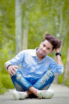 a young man sitting on the ground with his hands behind his head and looking at the camera