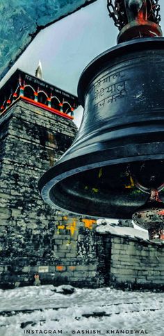 a large metal bell hanging from the side of a building with snow on the ground