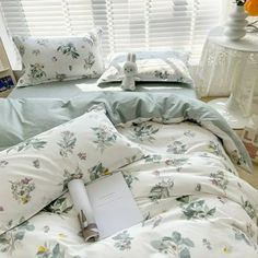 a book is laying on the bed next to pillows and pillowcases with flowers