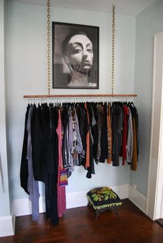 a closet with clothes hanging on the wall and a framed photo above it, along with an ottoman