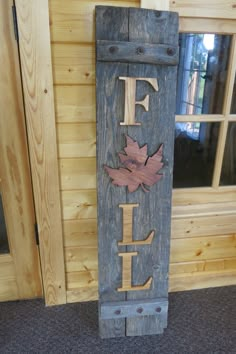 a wooden sign with the word fall painted on it in front of a log cabin