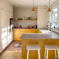 a kitchen with yellow cabinets and white stools