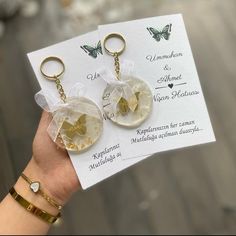 a person holding two key chains in front of a piece of paper with butterflies on it