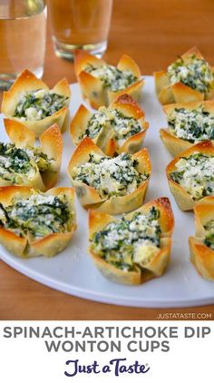 small appetizers with spinach and cheese are on a white plate next to two glasses