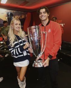 a man standing next to a woman holding a large silver trophy in front of her