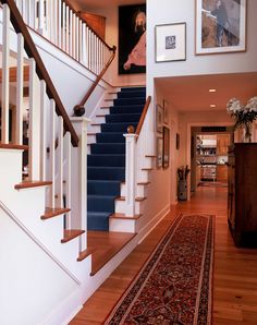 a staircase with blue carpet and pictures on the wall next to it, along with an area rug