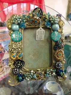 an ornate gold frame with blue and green beads on the edges is sitting on a glass table