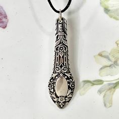 an ornate spoon is hanging from a cord on a white surface with flowers in the background