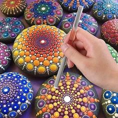 a hand is holding a pen and drawing on some rocks with different colors, shapes and sizes