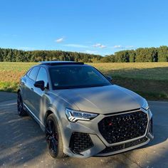 the front end of a silver car parked in a parking lot next to a field