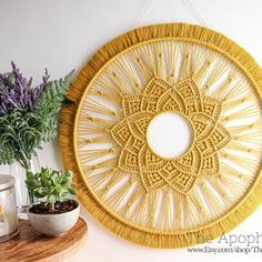 a yellow wall hanging on the side of a white wall next to potted plants