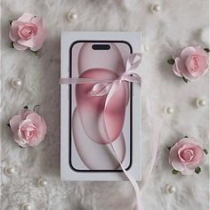 an iphone case in the packaging with pink roses around it on a white blanket and pearls