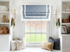 a window seat with two pillows on it in front of a white wall and shelves