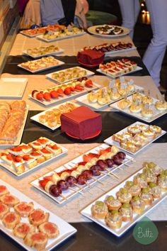 a table topped with lots of trays of food next to people standing behind it