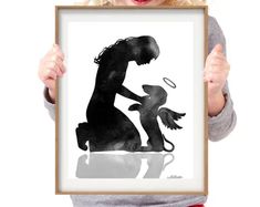 a woman holding up a framed black and white poster with a silhouette of a man kneeling down next to a dog