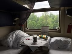 two beds in a small room with a table on one side and trees outside the window