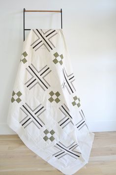 a white and green blanket hanging on a wall next to a wooden floor with an iron frame