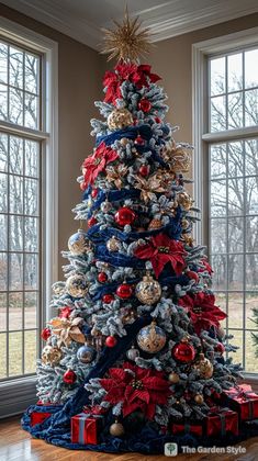 a christmas tree decorated with red, white and blue ribbons in front of two windows