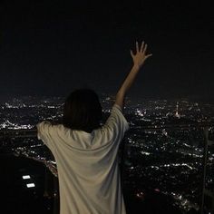 a person standing on top of a building at night with their arms in the air