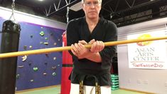 a man standing in front of a wall with climbing ropes on it and holding onto a pole