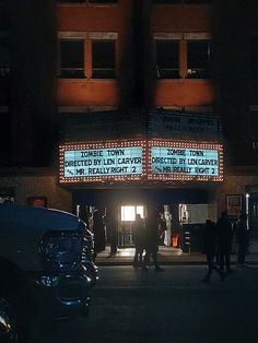 people are standing in front of the theater marquee at night with lights on